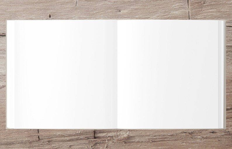 May include: A blank, white, open book lying flat on a light brown wooden surface.