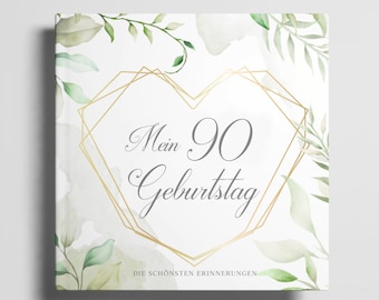 May include: A white book cover with a gold heart-shaped frame and green watercolor leaves. The text "Mein 90 Geburtstag" is inside the frame. The text "DIE SCHÖNSTEN ERINNERUNGEN" is at the bottom of the cover.