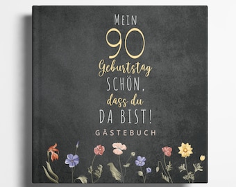 May include: A black chalkboard with the text "Mein 90 Geburtstag schön, dass du da bist! Gästebuch" in gold lettering. The chalkboard is decorated with a border of colorful flowers.