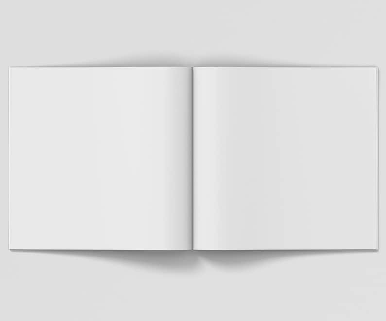 Puede incluir: Un libro blanco abierto, en blanco, con un lomo en el centro. El libro est&aacute; acostado sobre una superficie blanca.