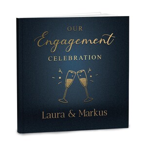 Könnte beinhalten: Ein quadratisches Fotobuch mit einem dunkelblauen Einband, der mit goldenem Text bedruckt ist: OUR Engagement CELEBRATION und Laura & Markus. Das Design zeigt eine goldene Strichzeichnung von zwei aneinanderstoßenden Champagnergläsern.