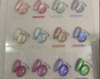 May include: A clear display board labelled KAISE NAIL featuring 12 colour samples of nail polish. Each sample includes an oval nail tip and a round cabochon in matching iridescent, metallic, and cat-eye finishes, ranging from pink to green.