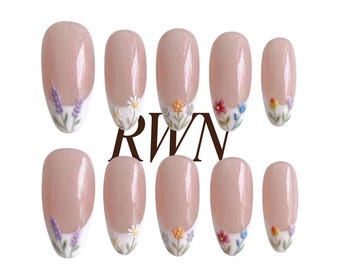May include: A set of ten almond-shaped press-on nails with a nude base and white French tips. Each nail features a small, delicate floral design in various colours including purple, white, orange, and red. The text RWN is centred between the rows.