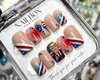 May include: A set of ten press-on nails in a clear plastic case labelled NAILBOX FOR YOU. The nails feature a nude base with red, white, and blue patriotic designs, including stars, stripes, a bow, and a portrait of Donald Trump giving a thumbs up.