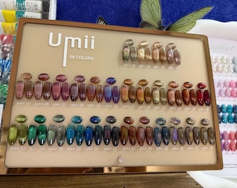 May include: A rectangular display board labelled Umii 28 Colors featuring twenty-eight oval nail polish samples with cat-eye effects. The samples are arranged in rows, showcasing a variety of metallic, iridescent, and deep jewel-toned shades.