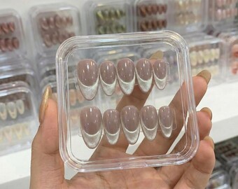 May include: A set of ten almond-shaped press-on nails in a clear plastic storage case. Each nail features a glossy nude base with a shimmering silver cat-eye magnetic polish tip, creating a modern take on a classic French manicure design.