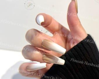 May include: A hand showing long, square press-on nails with a gradient design, shifting from light beige to white. The thumb nail is solid white. The text "Pinnacle Handmade Soft Gel Press On Nails" is visible on the image.