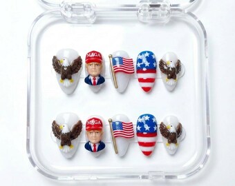 May include: A set of ten press-on nails in a clear plastic case. The designs include a 3D brown eagle on a white base, a 3D figure of a person wearing a red MAGA hat, a 3D American flag on a gold pole, and a red, white, and blue star-striped pattern.