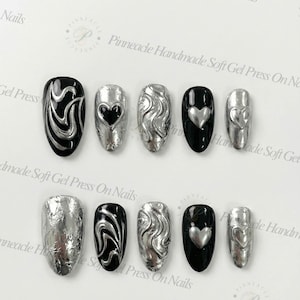 Puede incluir: Un conjunto de uñas postizas con varios diseños. Algunas uñas son negras con remolinos plateados o corazones. Otras son plateadas con superficies texturizadas. El texto "Pinnacle Handmade Soft Gel Press On Nails" es visible.