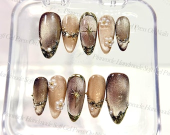May include: A set of press-on nails in a clear plastic case. The nails have a gradient design with gold glitter, decorated with pearls and gold details. Some nails feature a star design.