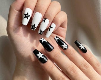 May include: Long coffin-shaped artificial nails featuring a high-contrast black and white colour scheme. The design alternates between white nails with black star motifs and black nails with white star motifs, each accented with a small central rhinestone.