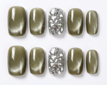 May include: A set of ten press-on nails arranged in two rows. Eight nails feature a smooth, olive green cat-eye finish with a reflective shimmer. Two central nails are covered in a dense, textured layer of silver, multifaceted glitter pieces.