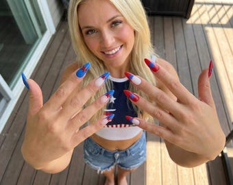 May include: Long almond-shaped fingernails featuring a patriotic design with a white base, red and blue tips, and small blue or red star accents on each nail. The nails are styled with a glossy finish, showcasing a vibrant colour palette of red, white, and blue.
