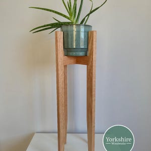 May include: A wooden plant stand with a light brown finish, holding a teal ceramic pot with a green aloe vera plant. The stand has a mid-century modern design. The plant stand is approximately 76 cm tall, ideal for indoor plants.