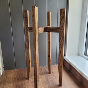 May include: A wooden plant stand with a dark brown stain. The stand has four legs and a square top.
