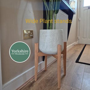 May include: A light grey speckled plant pot on a natural wood plant stand. The stand has a four-legged design. The text "Wide Plant stands" is in yellow. The Yorkshire Woodworks logo is in the lower left corner.