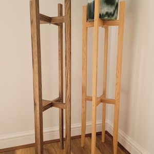 May include: Two wooden plant stands, one stained dark brown and one natural wood. Both stands have a square top and four legs.