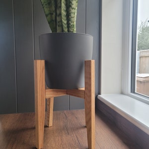 May include: A grey plant pot with a green snake plant sits on a wooden plant stand with four legs. The stand is made of natural wood and has a simple design.