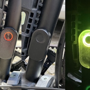May include: Close-up of a black bicycle lock with a red button. The lock is attached to a black bicycle frame. The button is illuminated in the third image, showing a green light.