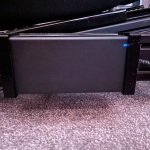 May include: A black power adapter with a blue light indicator mounted to a black metal frame.