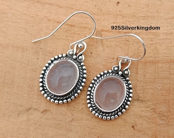 May include: A pair of silver earrings with a pink oval gemstone set in a beaded border. The earrings have a hook closure.