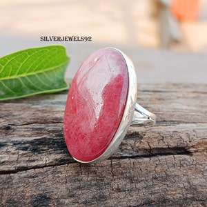 Peut inclure: Une bague en argent avec une grande pierre rouge de forme ovale. La bague est sertie dans une bande d'argent avec une finition lisse.