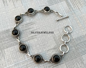May include: A silver bracelet with black onyx stones. The bracelet has a toggle clasp and a chain extender.