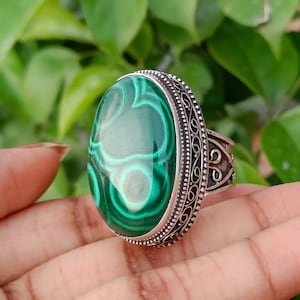May include: A silver ring featuring an oval green malachite stone set in an intricate filigree design.