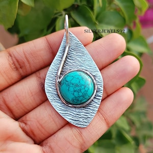 May include: A silver pendant featuring a turquoise stone set within a leaf-shaped design. The pendant has a textured surface and a silver wire detail.