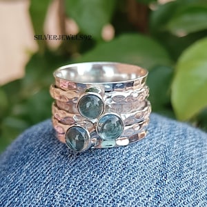 May include: A silver ring with three blue gemstones set in a hammered band. The ring is made of multiple bands that spin around each other.