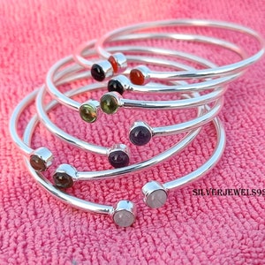 Pode incluir: Um conjunto de seis pulseiras de prata, cada uma com uma gema de cor diferente. As gemas são engastadas em engastes de prata e são vermelhas, pretas, verdes, roxas, marrons e brancas.