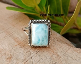 Könnte beinhalten: Ein Ring mit einem rechteckigen Larimar-Edelstein in einer gedrehten Silberfassung. Der Stein weist hellblaue und weiße Marmorierungen auf. Die Ringschiene ist aus poliertem Silber. Der Text 925Silverkingdom ist zu sehen.