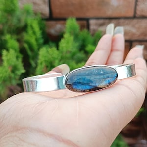 May include: A silver cuff bracelet with a large oval-shaped blue and brown gemstone set in the centre.