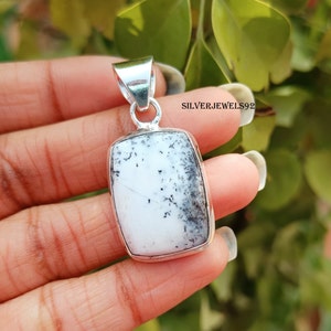 May include: A rectangular pendant with a white stone featuring black and grey inclusions, set in a silver metal frame. The pendant has a loop at the top for a chain. The text "SILVERJEWELS92" is visible.