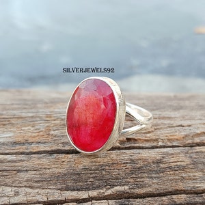 May include: A silver ring with a large, oval-shaped, red gemstone. The ring has a simple, elegant design.