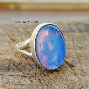 Op de afbeelding: Een zilveren ring met een ovale, blauw-roze steen. De steen heeft een wolkig, iriserend uiterlijk.