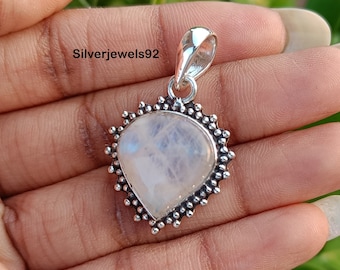 May include: A silver pendant with a white moonstone in a heart shape. The pendant has a silver bail and a decorative border of small silver beads.