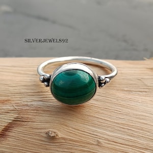 May include: A silver ring with a green malachite gemstone. The ring has a simple band with small decorative beads on each side of the stone.