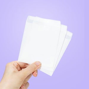May include: A hand holding three white envelopes, stacked on top of each other, against a light purple background.