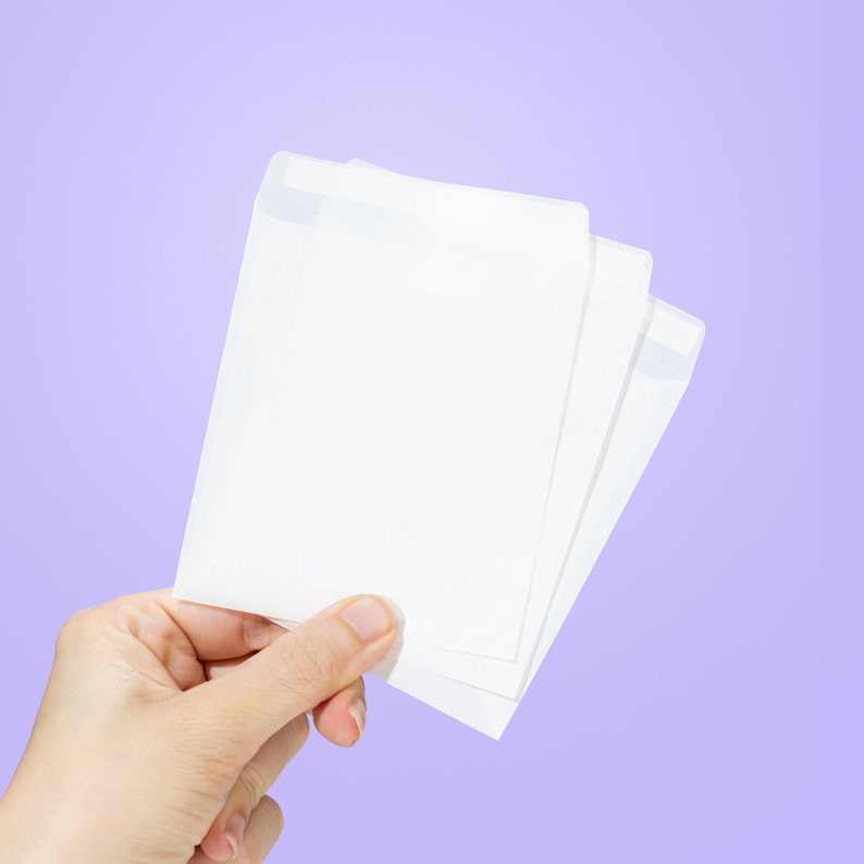 May include: A hand holding three white envelopes, stacked on top of each other, against a light purple background.
