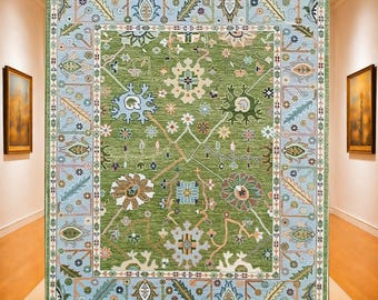 May include: A large, rectangular area rug with an intricate floral design. The rug features a central green field with a repeating pattern of flowers and leaves in shades of blue, brown, and cream. A light blue border frames the design.