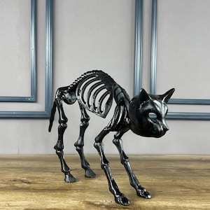 May include: A black cat skeleton figurine with a detailed rib cage, skull, and legs. The Halloween-themed decoration is posed in a stalking position on a wooden surface. The cat skeleton is approximately 10 inches long.