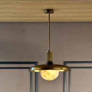 May include: A brass pendant light with a white alabaster globe shade. The light is hanging from a ceiling with wood paneling.