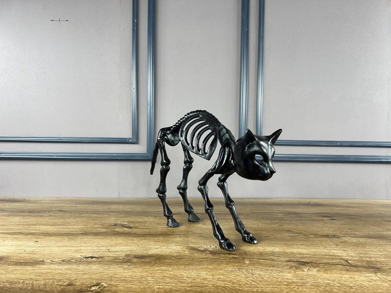 May include: A black cat skeleton ornament with a detailed rib cage, skull, and legs. The Halloween-themed decoration is posed in a stalking position on a wooden surface. The cat skeleton is approximately 25 cm long.