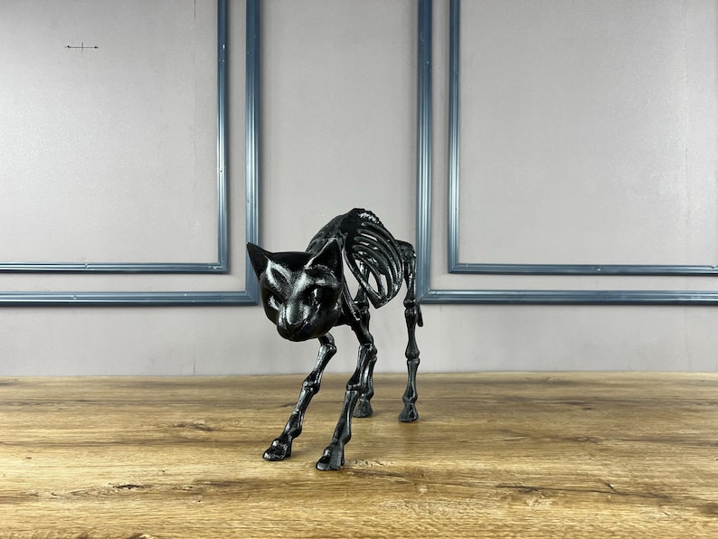 May include: A black cat skeleton ornament, featuring a detailed skeletal design. The cat is depicted in a stalking posture, with its head down and legs slightly flexed. The ornament is made of a glossy black material and rests on a wooden surface.