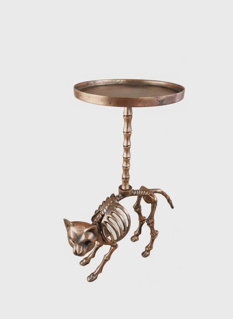 May include: A bronze-colored side table with a cat skeleton design. The table features a round top supported by a bamboo-style column, with the cat skeleton forming the base. A unique decorative accent.