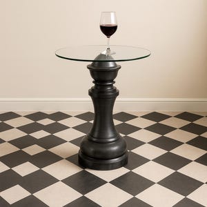 May include: A small, dark gray side table with a round glass top. A wine glass filled with red wine sits on the table. The table has a decorative, pedestal-style base. The floor has a black and white checkered pattern.