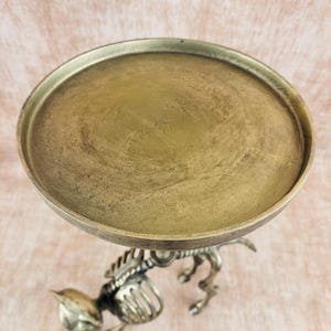 May include: A decorative, antique-style metal stand with a round, brass-colored tray. The stand is supported by a detailed, silver-colored cat skeleton design. The tray is approximately 8 inches in diameter.