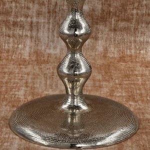 Pu&ograve; includere: Un supporto decorativo in metallo argentato con base rotonda e stelo a forma di clessidra. La base e lo stelo presentano un motivo a pois, che riflette la luce. Il supporto &egrave; progettato per contenere oggetti decorativi.
