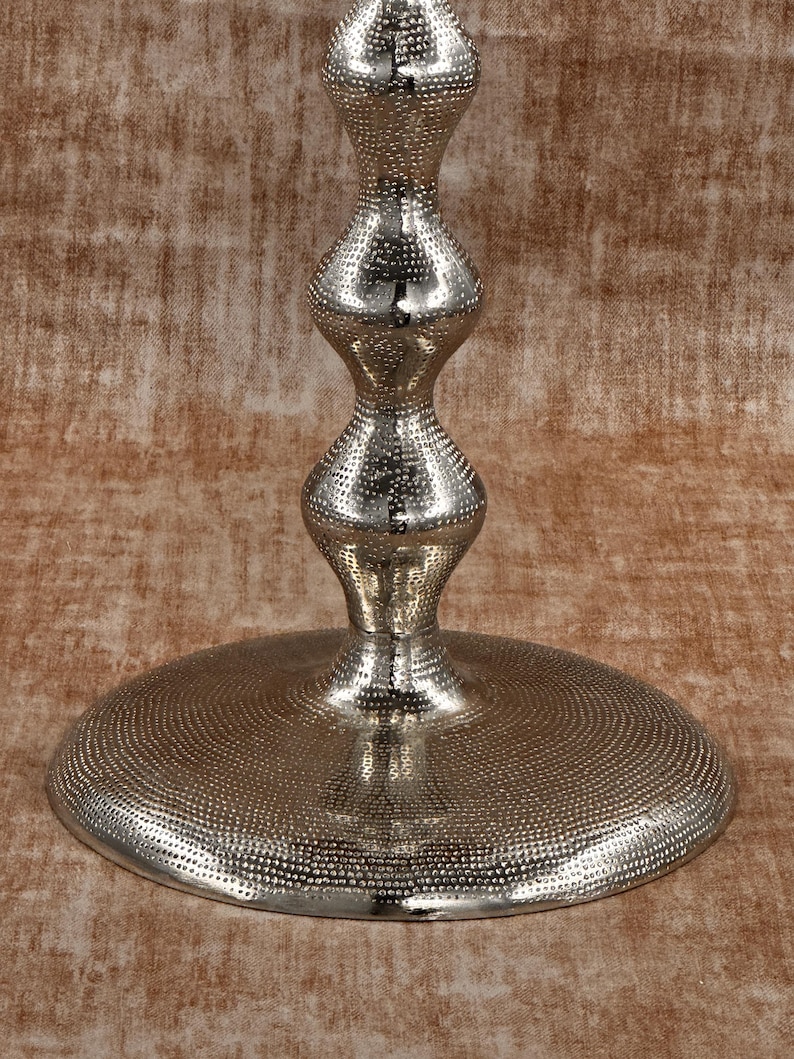 Pu&ograve; includere: Un supporto decorativo in metallo argentato con base rotonda e stelo a forma di clessidra. La base e lo stelo presentano un motivo a pois, che riflette la luce. Il supporto &egrave; progettato per contenere oggetti decorativi.